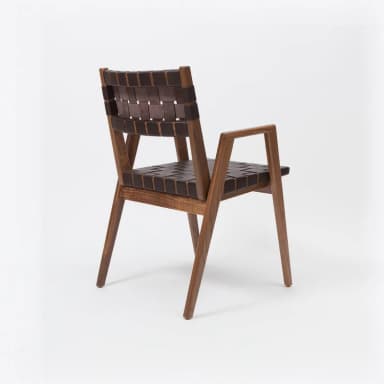 An armchair with a wooden frame and woven leather seat and backrest. The frame appears to be constructed from a dark wood, possibly walnut, with a natural finish. The seat and backrest are made of dark brown leather straps woven in a grid pattern. The chair has angled legs and minimalist armrests. — 3D model