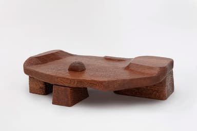 A unique, low-profile coffee table carved from wood. The tabletop features an organic, undulating surface with a textured finish, resembling natural erosion or flowing water. It is supported by four block-like legs, also made of wood. A single, small rectangular block rises from the center of the tabletop. The overall aesthetic is rustic and sculptural, with visible tool marks and a rich wood grain. — 3D model