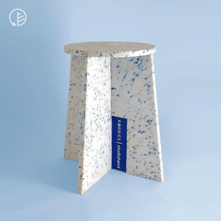 A compact side table featuring a round tabletop and three flat, angled legs, constructed from a light-colored material with multi-colored speckles, resembling recycled plastic or terrazzo. — 3D model