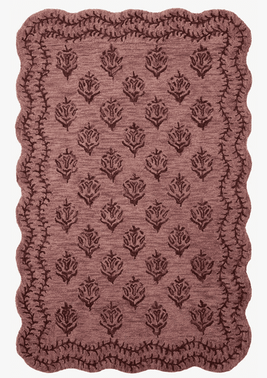 A small rectangular textile mat featuring a scalloped edge and an embossed or woven floral pattern across its surface. The mat is a muted brownish-mauve color, suggesting a soft, possibly plush texture. The floral motif consists of repeated rose-like designs arranged in a grid, contrasting subtly with the background texture. The edges are finished with a distinct scalloped border, adding a decorative touch. — 3D model