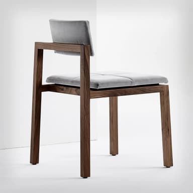 An armless chair featuring a light-toned wooden frame and cognac-colored leather upholstered seat and back cushions. Both the seat and back are divided into four square segments with visible stitching, creating a quadrille-tufted appearance. The wooden frame is simple and geometric, with straight legs and a low backrest support structure. — 3D model