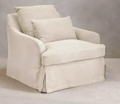 A light-colored, upholstered armchair featuring a loose slipcover design and a skirted base. It has wide, slightly rolled armrests and includes two loose, rectangular cushions for the seat and back, plus a smaller lumbar or accent cushion. The overall aesthetic is casual and comfortable. — 3D model