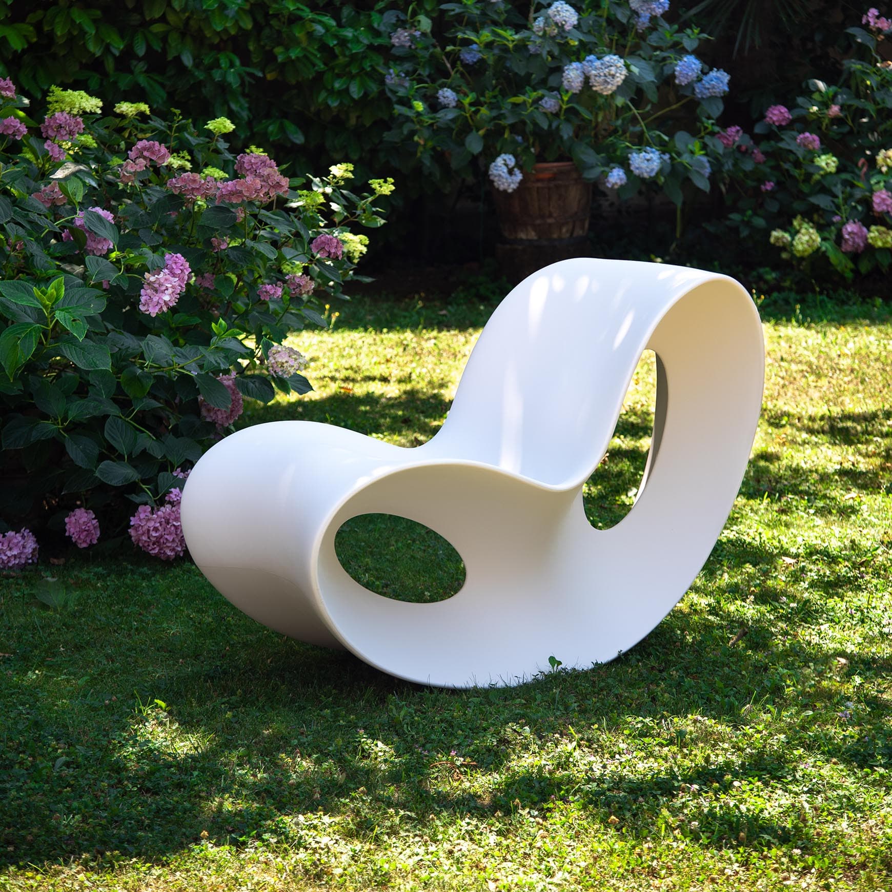 A pristine white modern sculptural rocking chair, featuring a continuous, organic form with hollowed-out sections that serve as visual design elements. The chair appears to be made from a single molded piece, offering a smooth, matte finish. — 3D model