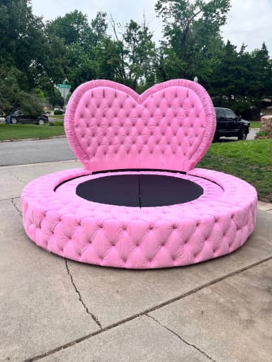 A lavish pink, round upholstered bed featuring deep button tufting across its entire frame and a distinctive heart-shaped headboard. The bed is upholstered in a soft, plush fabric, likely velvet, and the central sleeping area is recessed with a dark, possibly black, base. — 3D model