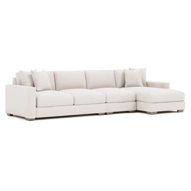 A contemporary sectional sofa, upholstered in a light-colored, textured fabric. It features a chaise lounge on the right side and comes with multiple throw pillows. The sofa has clean lines, plush cushions, and low-profile wooden legs. — 3D model