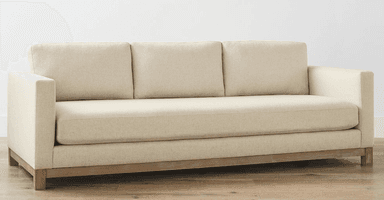 A three-seater sofa upholstered in a textured, light beige fabric. The sofa features a wooden base frame and legs, with a visible grain texture on the wood. The back of the sofa is designed with three separate cushions, and the side profile shows a clean, rectangular form. The overall aesthetic suggests a contemporary or transitional style. — 3D model
