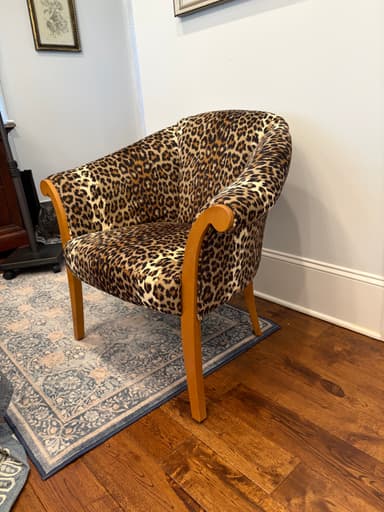 An armchair featuring full upholstery in a distinctive leopard print fabric, supported by visible wooden legs and armrest elements. The chair has a rounded back and seat, with the arms flowing into the front legs. — 3D model