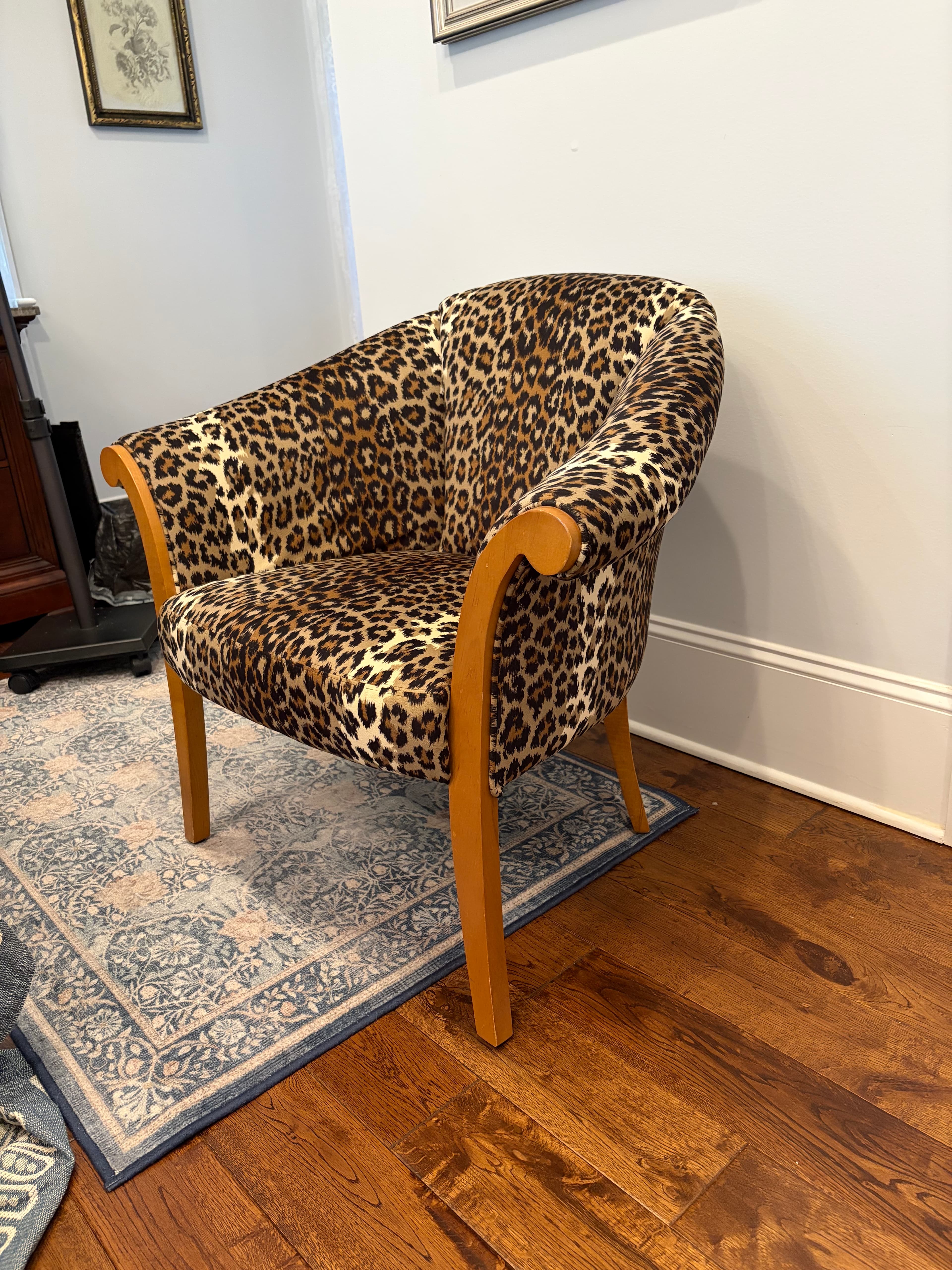 An armchair featuring full upholstery in a distinctive leopard print fabric, supported by visible wooden legs and armrest elements. The chair has a rounded back and seat, with the arms flowing into the front legs. — 3D model