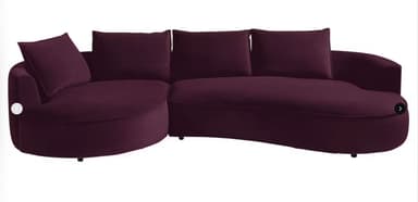 A large, contemporary curved sectional sofa featuring a deep purple fabric upholstery. The sofa includes an integrated round chaise lounge component on one end, transitioning into a curved seating section. It is furnished with multiple loose back cushions and accent pillows, all matching the deep purple upholstery. The design incorporates a low profile with recessed feet, giving it a floating appearance. — 3D model