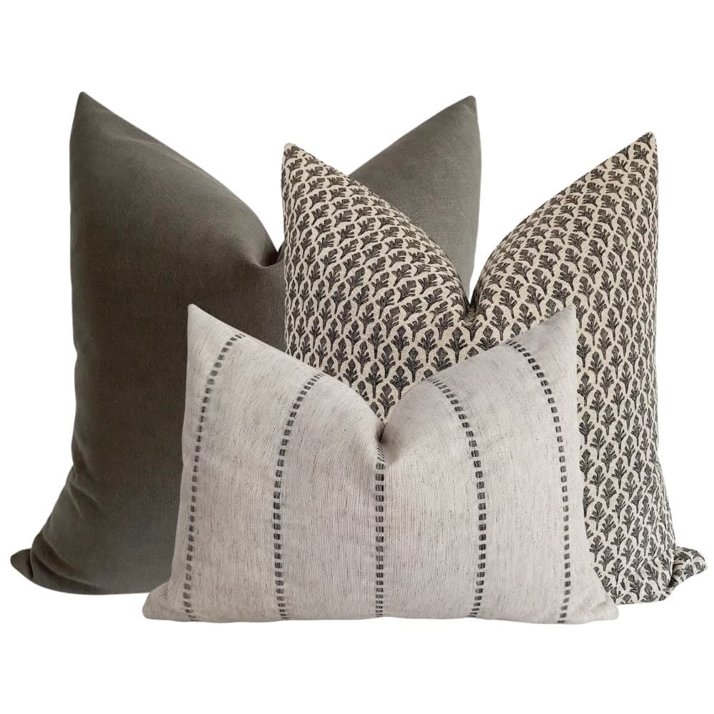 A set of three decorative throw pillows. One pillow is a solid dark grey, likely velvet or a similar soft fabric. Another pillow features a repeating pattern of dark brown stylized leaf motifs on a cream background. The third pillow is rectangular and oriented horizontally, with a textured cream fabric and vertical stripes composed of dashed lines in a dark grey or brown hue. The pillows are arranged in a layered composition. — 3D model