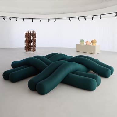 A contemporary low-profile ottoman constructed from multiple thick, tubular segments that are braided and intertwined, upholstered in a dark teal fabric. — 3D model