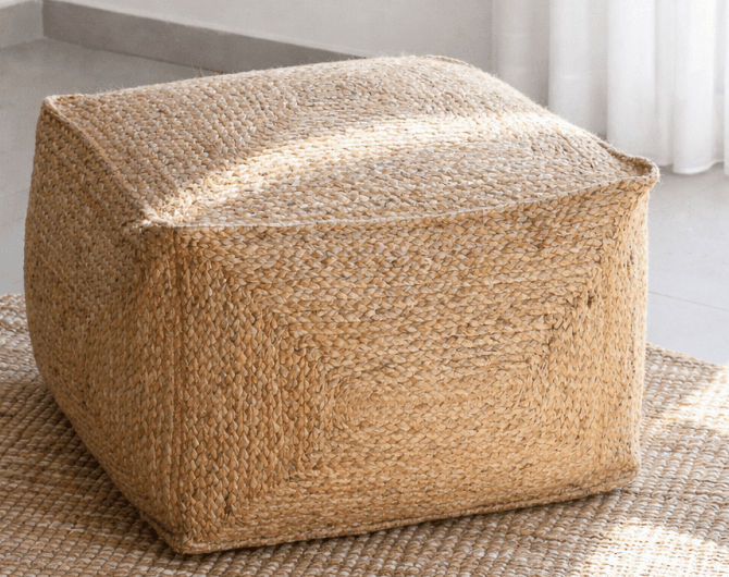 A square-shaped pouf ottoman covered in braided natural jute. The top surface features stitched seams that create a segmented, symmetrical pattern, reflecting the cube form. Its earthy color and textured surface give it a natural, bohemian aesthetic. — 3D model