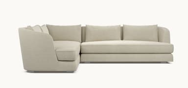 A modern sectional sofa with a light beige fabric upholstery. The sofa features a chaise lounge on the left and a sofa section on the right, with loose back cushions. The design is minimalist with clean lines and a low profile, supported by subtle metallic legs. — 3D model