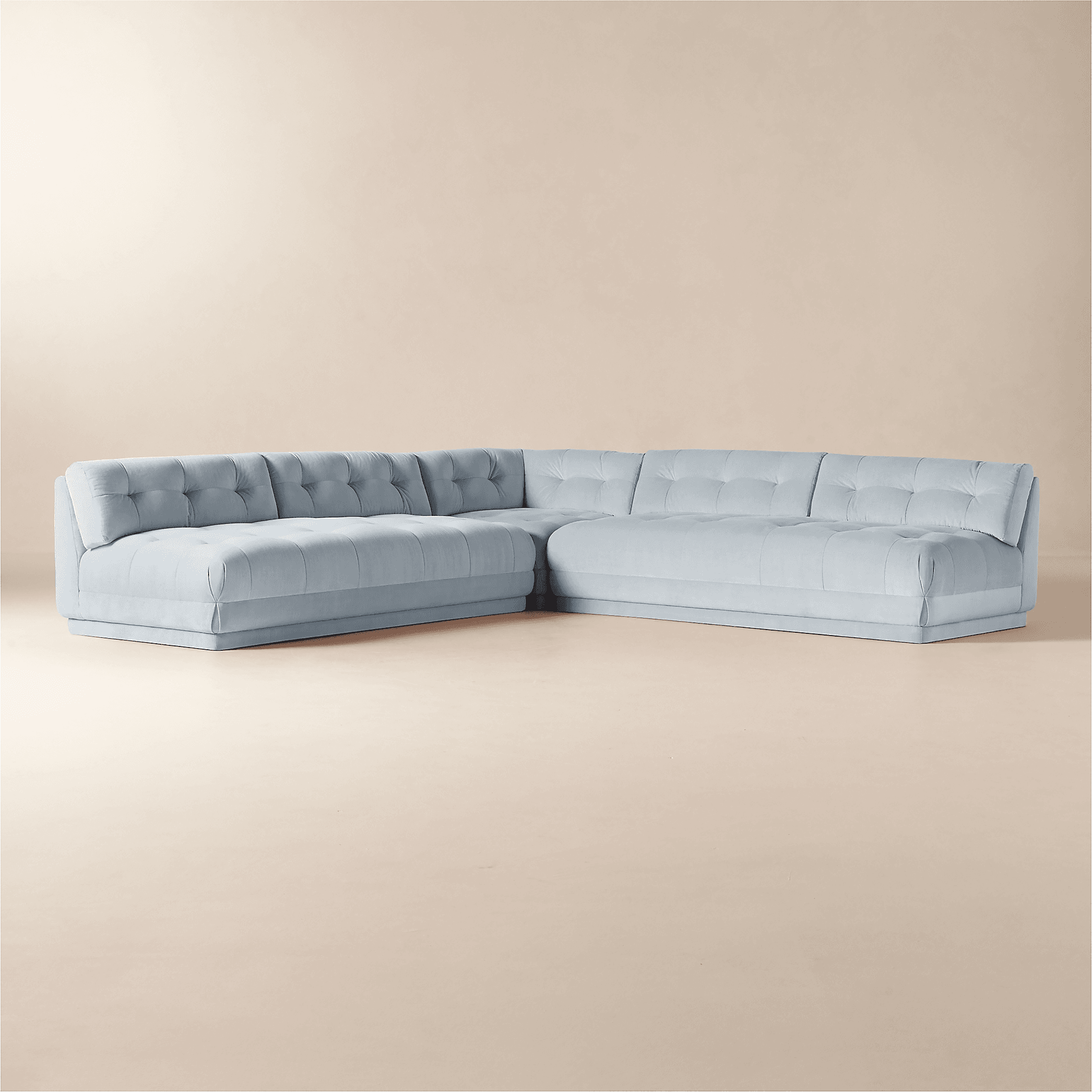 A light blue, tufted sectional sofa with a low profile and a modern design. The sofa features deep seats and padded arms. The tufting is present on both the seat and back cushions, creating a textured surface. The base is a continuous, flat panel that gives the sofa a streamlined appearance. It is arranged in an 'L' shape, indicating it is composed of multiple connected modules. — 3D model