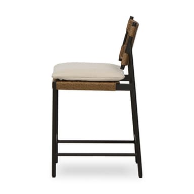 A contemporary bar stool featuring a dark-colored metal frame, a woven synthetic rattan seat and backrest, and a light-colored fabric cushion. The stool includes an integrated footrest for comfort. The backrest has cut-out handles on either side, and the overall aesthetic is clean and modern, suggesting suitability for both indoor and outdoor environments. — 3D model