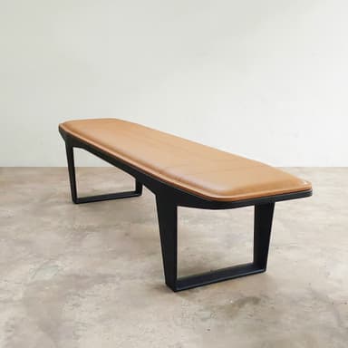 A long, rectangular bench featuring a padded, tan upholstered seat with stitched detailing, supported by a minimalist black metal frame with inverted V-shaped legs. — 3D model
