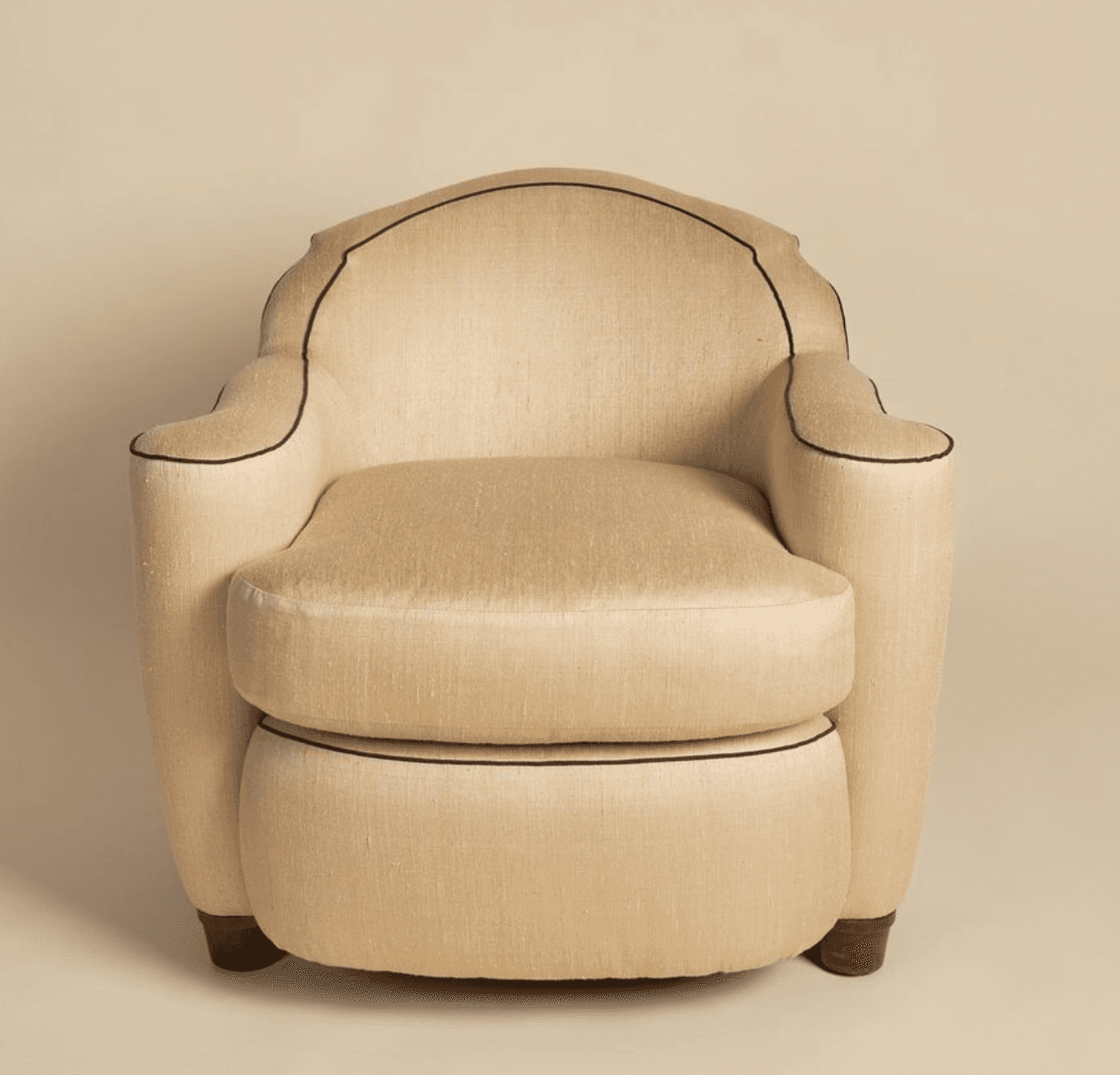 An upholstered armchair featuring a rounded, club-style silhouette with prominent piping. The chair is covered in a light, neutral fabric and has a separate, plump seat cushion. Its back and arms curve smoothly, and dark brown piping accentuates the contours of the chair, including the backrest, armrests, and the base of the seat cushion. The armchair is supported by short, dark wooden tapered legs. — 3D model