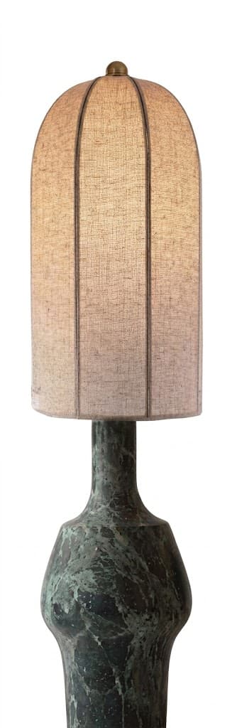 A distinctive table lamp featuring a heavily patinated, sculptural metal base in a dark green-bronze hue, supporting a tall, arched fabric shade. The base has an organic, fluid shape with a narrower neck and a wider, bulbous lower section, suggesting a lost-wax casting or hammered finish with natural oxidation. The shade is a light, neutral-toned linen or similar textile, with visible vertical ribs or seams, culminating in a rounded dome at the top. A small, brass-toned finial secures the shade. The lamp emits a warm, diffused light. — 3D model
