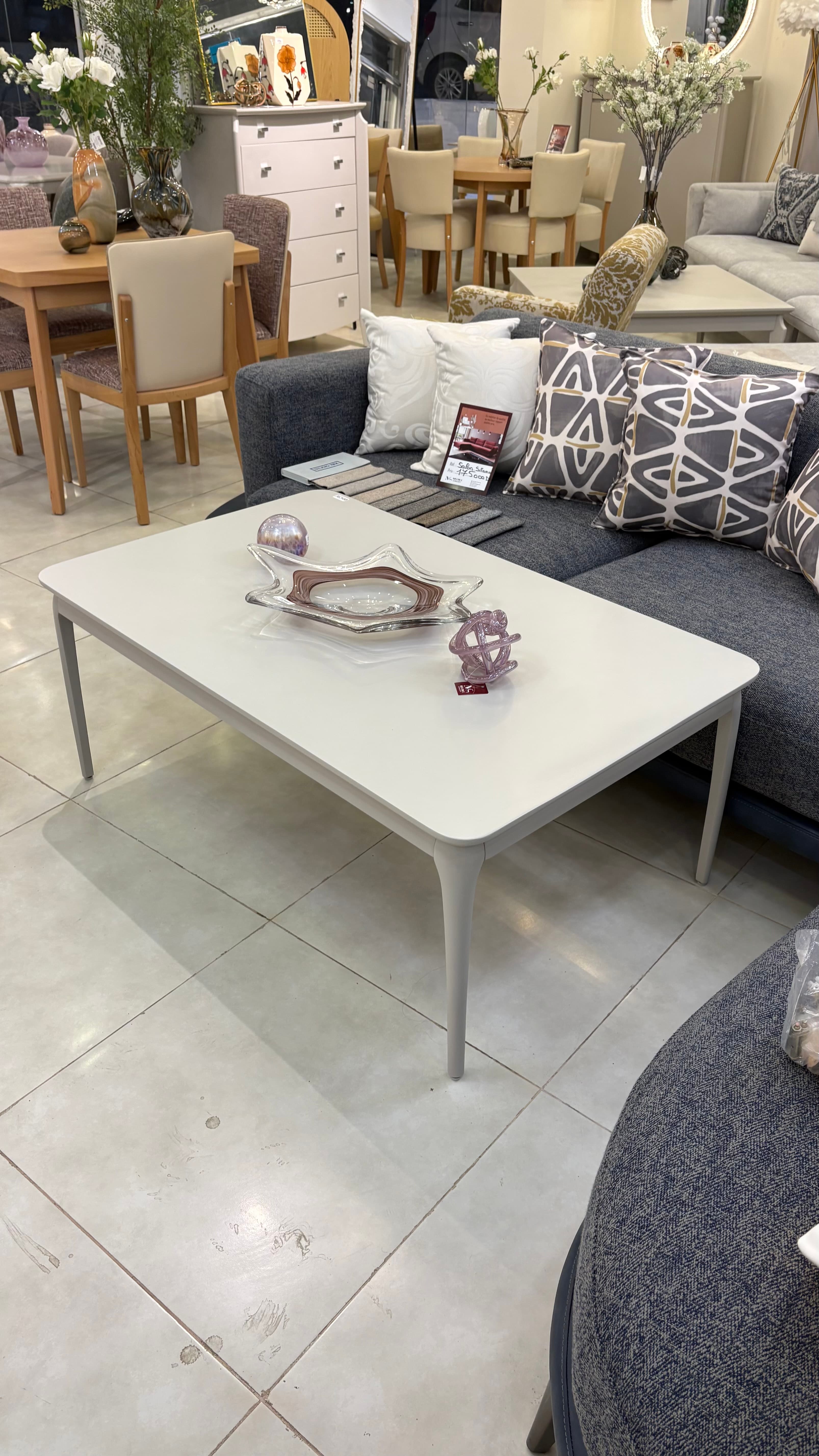 A modern rectangular coffee table featuring a light grey or off-white tabletop with softly rounded corners, supported by four subtly tapered legs matching the tabletop's color and finish. — 3D model