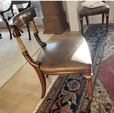 A classical side chair with a dark wood frame and a brown upholstered seat. The chair features a curved backrest supported by turned uprights that incorporate fluted golden accents. The seat is rectangular and upholstered in what appears to be leather, fastened with brass studs along the edge. The wooden legs are turned and feature decorative golden elements near the seat. The overall design evokes a traditional or neoclassical style. — 3D model