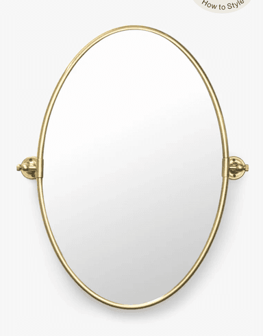 An oval-shaped mirror featuring a slender, polished brass-tone metal frame. The mirror is designed for wall mounting and includes a pivoting mechanism on both sides, allowing it to tilt for adjustable viewing angles. The mounting hardware is also finished in polished brass, matching the frame. — 3D model