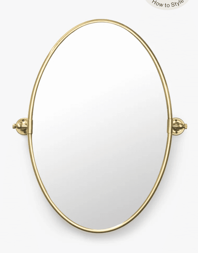 An oval-shaped mirror featuring a slender, polished brass-tone metal frame. The mirror is designed for wall mounting and includes a pivoting mechanism on both sides, allowing it to tilt for adjustable viewing angles. The mounting hardware is also finished in polished brass, matching the frame. — 3D model