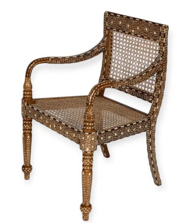 An Anglo-Indian style armchair featuring a dark-stained wooden frame extensively decorated with intricate bone or ivory inlay. It has a woven cane seat and a matching cane backrest. The arms are curved and inlaid, and the front legs are turned with ornate carvings, terminating in bun feet. The overall design is highly decorative and showcases traditional craftsmanship. — 3D model