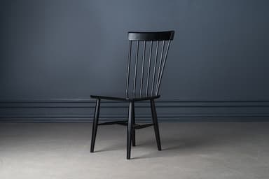 A classic black lacquered Windsor-style dining chair, featuring a tall spindle backrest and a solid wood saddle-shaped seat. The chair stands on four splayed and tapered legs, reinforced by H-stretchers, offering a timeless and sturdy design. — 3D model