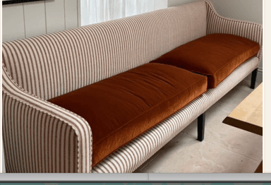 A two-seater upholstered settee featuring a high back, slightly flared arms, and four dark, tapered legs. The frame is covered in a striped fabric, complemented by solid reddish-brown seat cushions, and finished with decorative nailhead trim. — 3D model