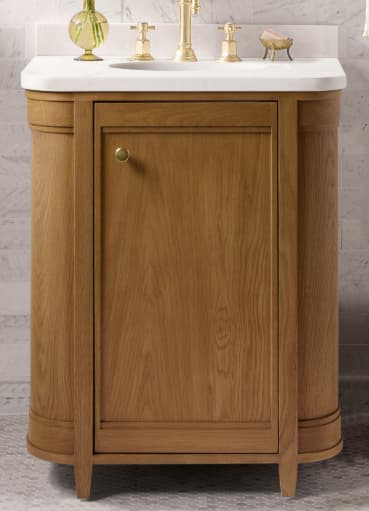 A freestanding bathroom vanity featuring a natural light-toned wooden cabinet with decorative paneling and rounded vertical details, topped with a bright white integrated sink basin and equipped with a widespread brass-finished faucet and matching knob handles. — 3D model