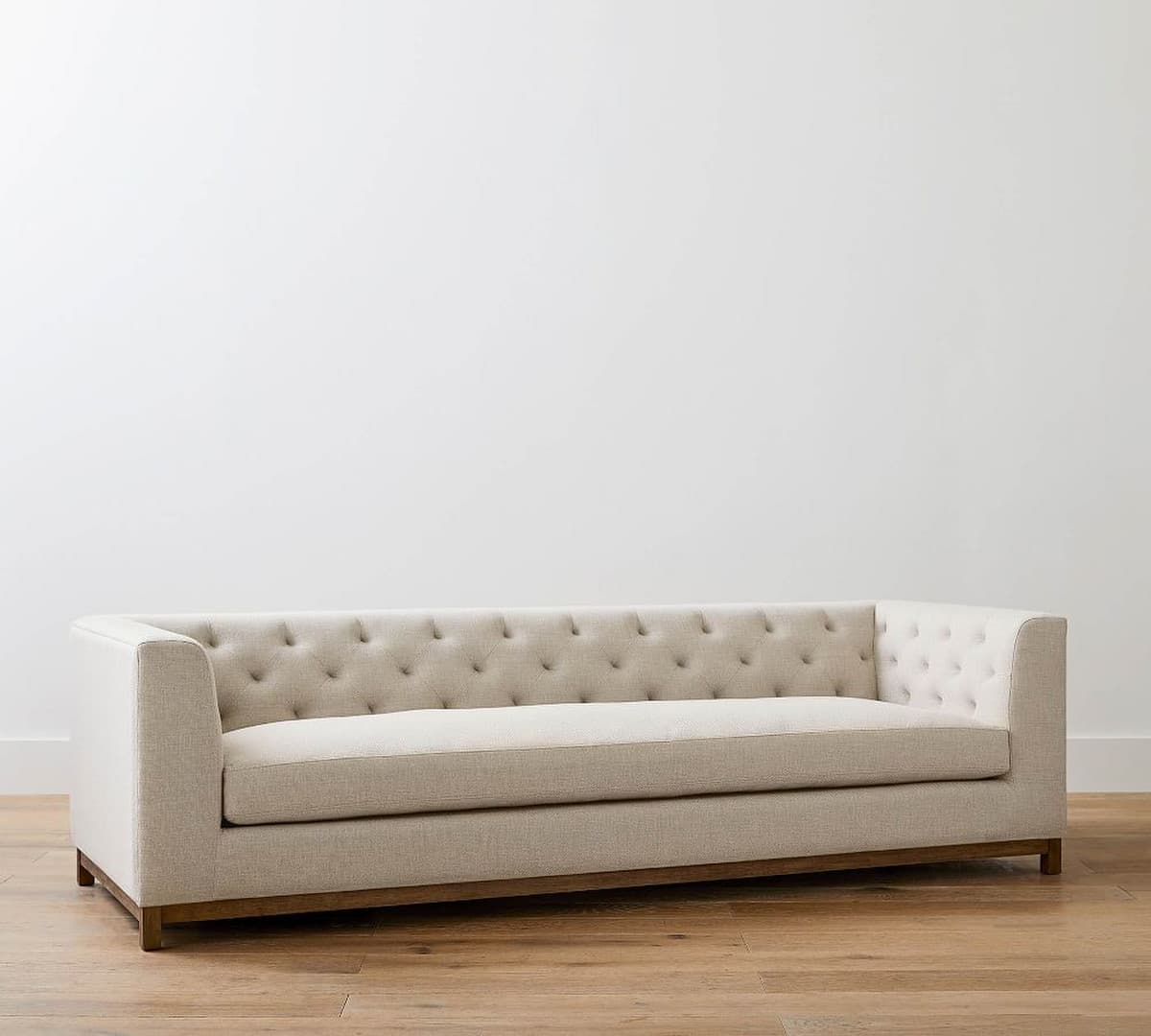 A modern three-seater sofa featuring light beige linen upholstery with a button-tufted backrest and arms, and an exposed dark wood base. — 3D model