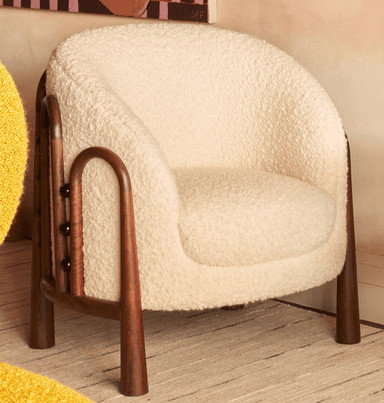 A contemporary accent armchair featuring a rounded, upholstered body covered in a cream-colored, textured boucle-like fabric. The chair has exposed dark wood elements that form the armrests and extend downwards to become the tapered legs. The design emphasizes soft curves and a minimalist aesthetic. — 3D model