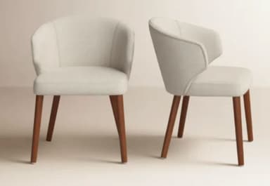 A contemporary upholstered armchair featuring a continuous, curved backrest that seamlessly transitions into integrated armrests. The chair is fully upholstered in a light, neutral-toned fabric, likely cream or off-white. It stands on four slender, round, and outwardly tapered wooden legs with a dark brown finish. The overall design emphasizes a compact and modern aesthetic. — 3D model