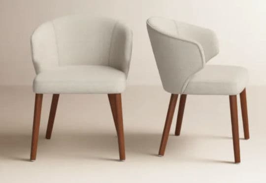 A contemporary upholstered armchair featuring a continuous, curved backrest that seamlessly transitions into integrated armrests. The chair is fully upholstered in a light, neutral-toned fabric, likely cream or off-white. It stands on four slender, round, and outwardly tapered wooden legs with a dark brown finish. The overall design emphasizes a compact and modern aesthetic. — 3D model