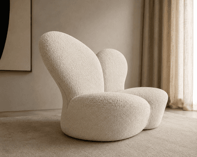 A sculptural, low-profile lounge chair upholstered in cream-colored bouclé fabric. The chair features a distinct organic form with smooth, continuous curves forming the seat, back, and integrated armrests. Its plush appearance suggests comfort, and the overall design is contemporary and minimalist, resting directly on the floor without visible legs. — 3D model