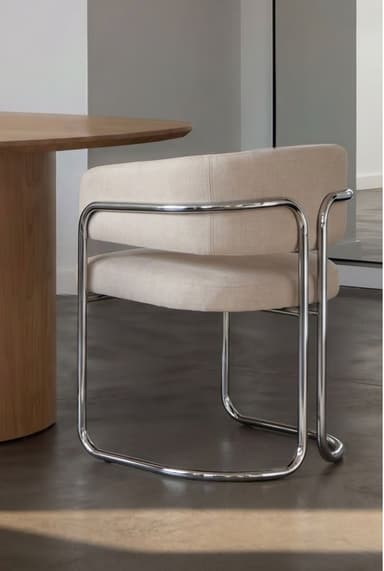 A modern armchair featuring a tubular chrome frame and upholstered in a light, neutral fabric. The seat and backrest are well-cushioned, and the back curves around to form integrated armrests. A polished chrome bar accentuates the exterior of the armrests, connecting to the continuous loop base. — 3D model