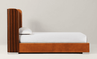 A contemporary platform bed featuring a tall, curved headboard with vertical fluted cognac leather upholstery, flanked by dark wood side panels. The bed frame is also upholstered in matching cognac leather, resting on polished metal block feet. — 3D model