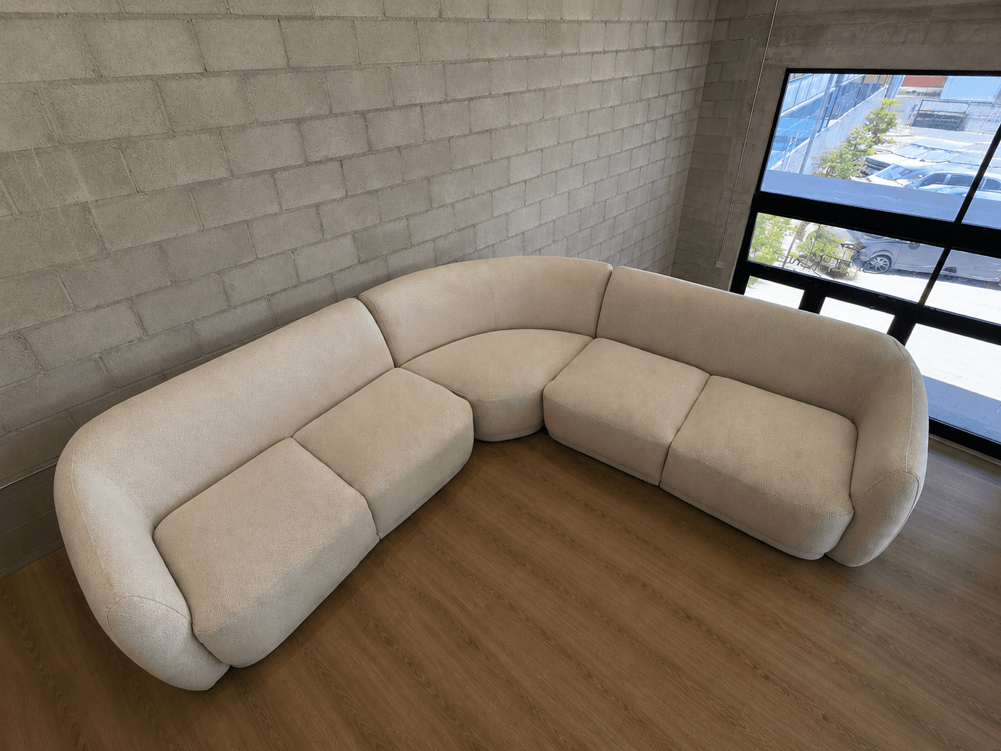 A large, modular sectional sofa forming an L-shape, featuring gently curved sections and rounded arms and backrests. It is upholstered in a light, textured fabric, giving it a contemporary and soft appearance. The sofa appears to be composed of multiple interchangeable units. — 3D model