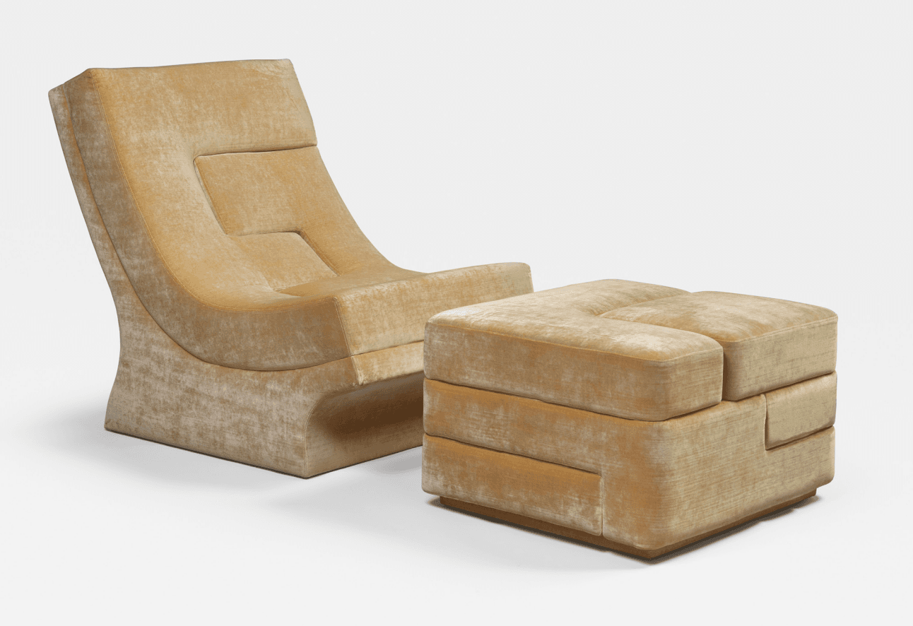 A contemporary lounge chair and ottoman set upholstered in a plush, textured velvet fabric. The chair features a high, reclined backrest with segmented cushioning and a sculptural, flowing base. The accompanying ottoman is cubic in form, with similar segmented cushioning and a visible wooden base. — 3D model