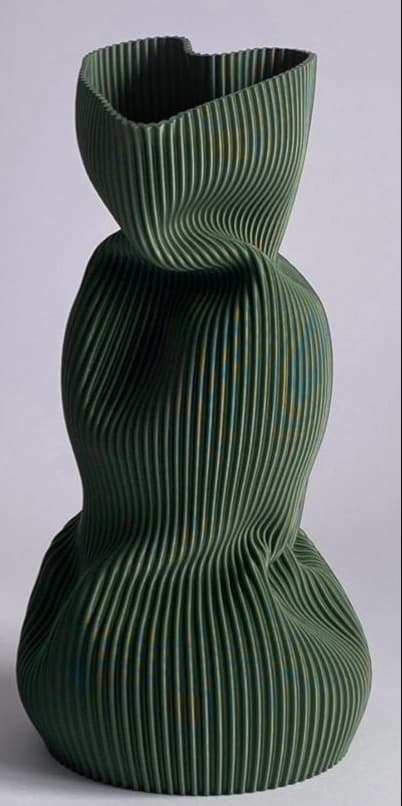 A tall, sculptural vase or decorative object featuring a distinctive pleated, ribbed texture across its entire surface. The form is organic and sinuous, with a wider base narrowing to a constricted waist before flaring out again towards the top, which has an asymmetrical opening. The color is a muted, dark green with subtle variations and undertones of lighter green, yellow, and blue, suggesting a complex glaze or finish. The overall aesthetic is modern and artistic, emphasizing form and texture. — 3D model