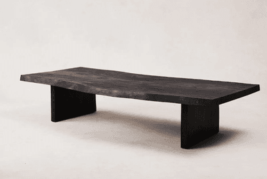 A low, rectangular coffee table with a live-edge top and thick, blocky legs. The tabletop has an irregular, natural edge on one side, and the surface displays visible wood grain. The legs are positioned inset from the ends of the tabletop. — 3D model
