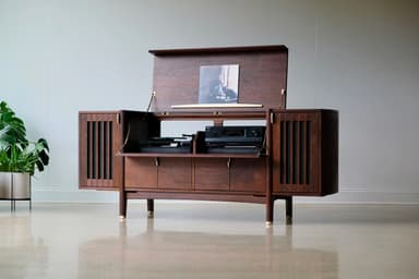 A long, low, dark wooden cabinet with a distinct mid-century modern design. It features slatted sections on the curved ends, a central open shelf, and multiple drawers and cabinet doors below, all adorned with small brass pull handles. The cabinet is supported by angled, tapered legs with brass ferrules at the bottom. — 3D model