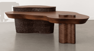 A sculptural, multi-tiered coffee table crafted from dark walnut wood. It features an organic, freeform tabletop with a smaller, raised circular platform on one end, and an integrated, slightly raised heart-shaped detail on the main surface. The table is supported by two distinct bases: a large, textured chiseled base with a roughly cylindrical form, and a smaller, smooth cylindrical leg with a subtle undulating wavy profile. The overall design emphasizes natural forms and contrasting textures. — 3D model