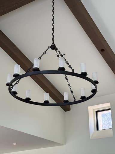 A black circular chandelier with a rustic or traditional design, suspended by a heavy-duty black chain. It features twelve cylindrical frosted glass shades arranged around the perimeter of the circular frame. The structure is made of metal with visible links in the chain and supporting arms. — 3D model