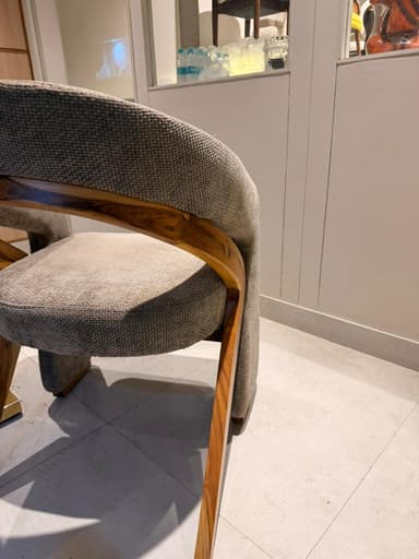 A contemporary armchair with a curved backrest and upholstered seat and arms. The frame appears to be constructed from wood, visible as a curved piece supporting the backrest. The upholstery is a textured fabric in a neutral tone. — 3D model