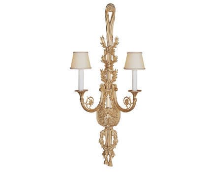 A classical-style double-armed wall sconce, predominantly gold in color, featuring intricate detailing reminiscent of acanthus leaves and lyre motifs. It is designed to hold two lights, each topped with a cream-colored, conical lampshade. — 3D model