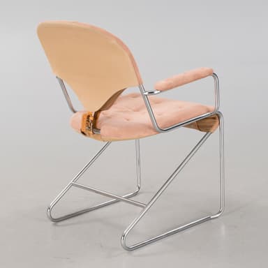 A cantilever armchair with a tubular chrome-plated steel frame. The seat, backrest, and armrests are upholstered in a tufted, salmon-pink, velvety fabric. The backrest has a distinct curved shape and is attached to the frame with leather straps. The armrests are also padded and follow the curvature of the frame. — 3D model
