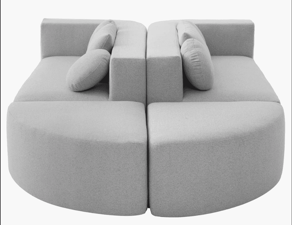 A modular, contemporary sofa composed of four curved and rectangular sections. The sofa features a light grey upholstered finish and includes two decorative pillows. The design emphasizes soft, rounded edges and a unified, cohesive appearance when assembled. — 3D model