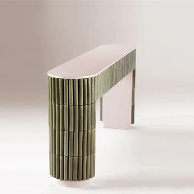 An elongated, narrow console table featuring a light pinkish-beige top and structural elements. The front and sides are extensively clad with vertical, muted green cylindrical elements, likely ceramic rods, creating a fluted or reeded texture. The base of the table follows the same pinkish-beige tone and features a subtle arched shape. — 3D model