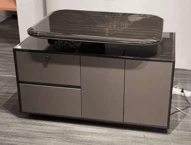 A modern credenza featuring a dark wood veneer finish on its main body and a contrasting matte grey/taupe on its drawer and cabinet door fronts. A distinctive curved-edge top piece, also in dark wood veneer, appears to float above the main structure, adding a contemporary design element. The unit includes one lockable drawer and two cabinet doors, suggesting practical storage functionality. — 3D model